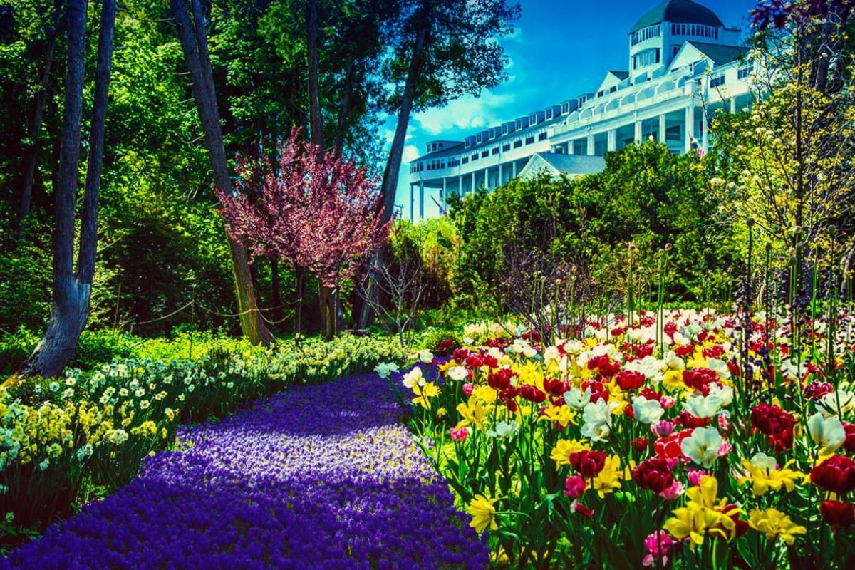 Garden at the Grand Hotel on Mackinac Island with red, yellow, pink, white, and purple flowers, green trees, and the top of the hotel in the background