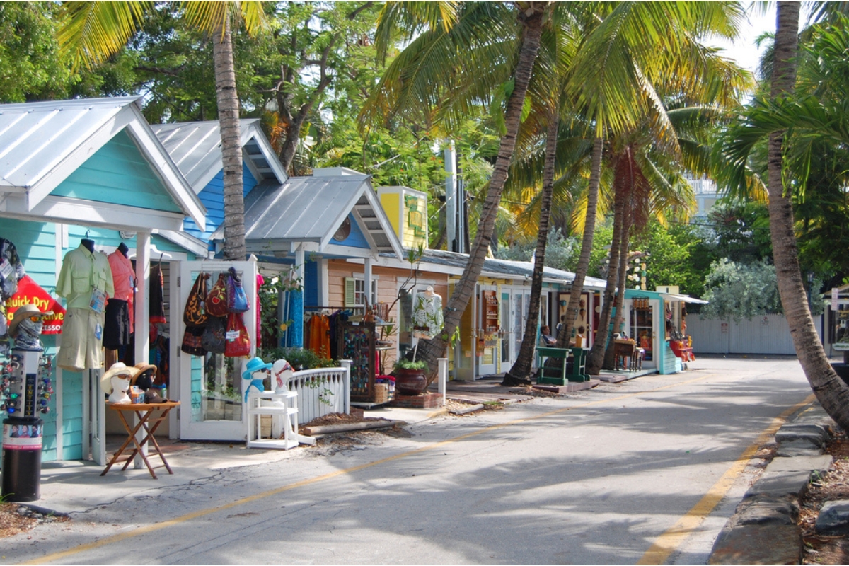 Small, narrow side street in Key West, lined with palm trees and white-roofed, pastel-colored cottages that are now boutique shops 