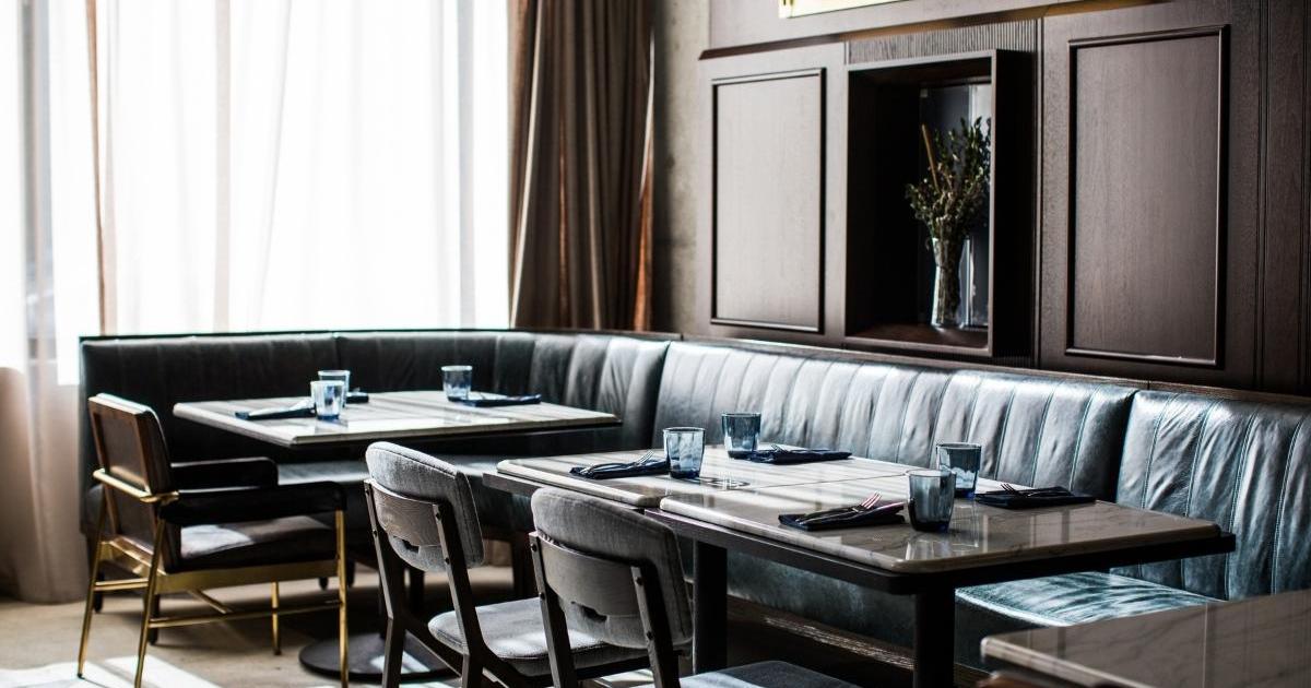 Dining room at the Marsh House restaurant at the Thompson Nashville Hotel. Decor is blue and brown with booths, tables, chairs, and large window lined with sheer curtains