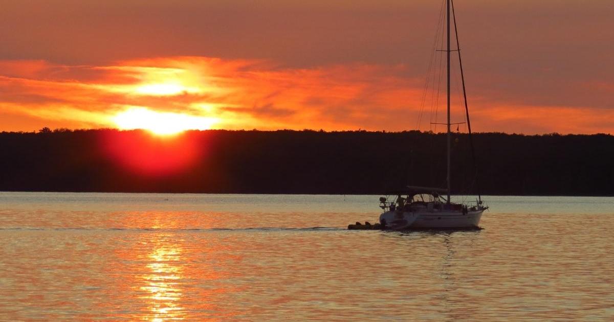 Boat with sails down, floating on water at sunset